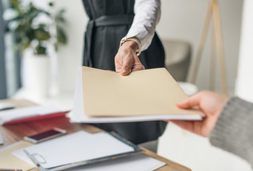 cropped shot of businesswoman giving envelope to colleague at workplace