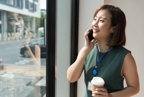 young Asian business woman talking on phone in office and hold coffee cup
